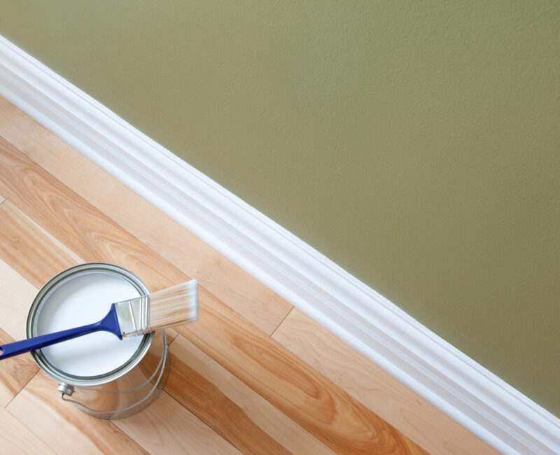 Newly opened can of white paint and paintbrush on wooden floor.